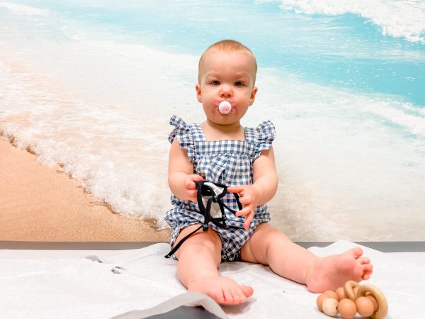 A baby posing in front of a beach background, made to look like the child is perched happily in the sand instead of on an exam table